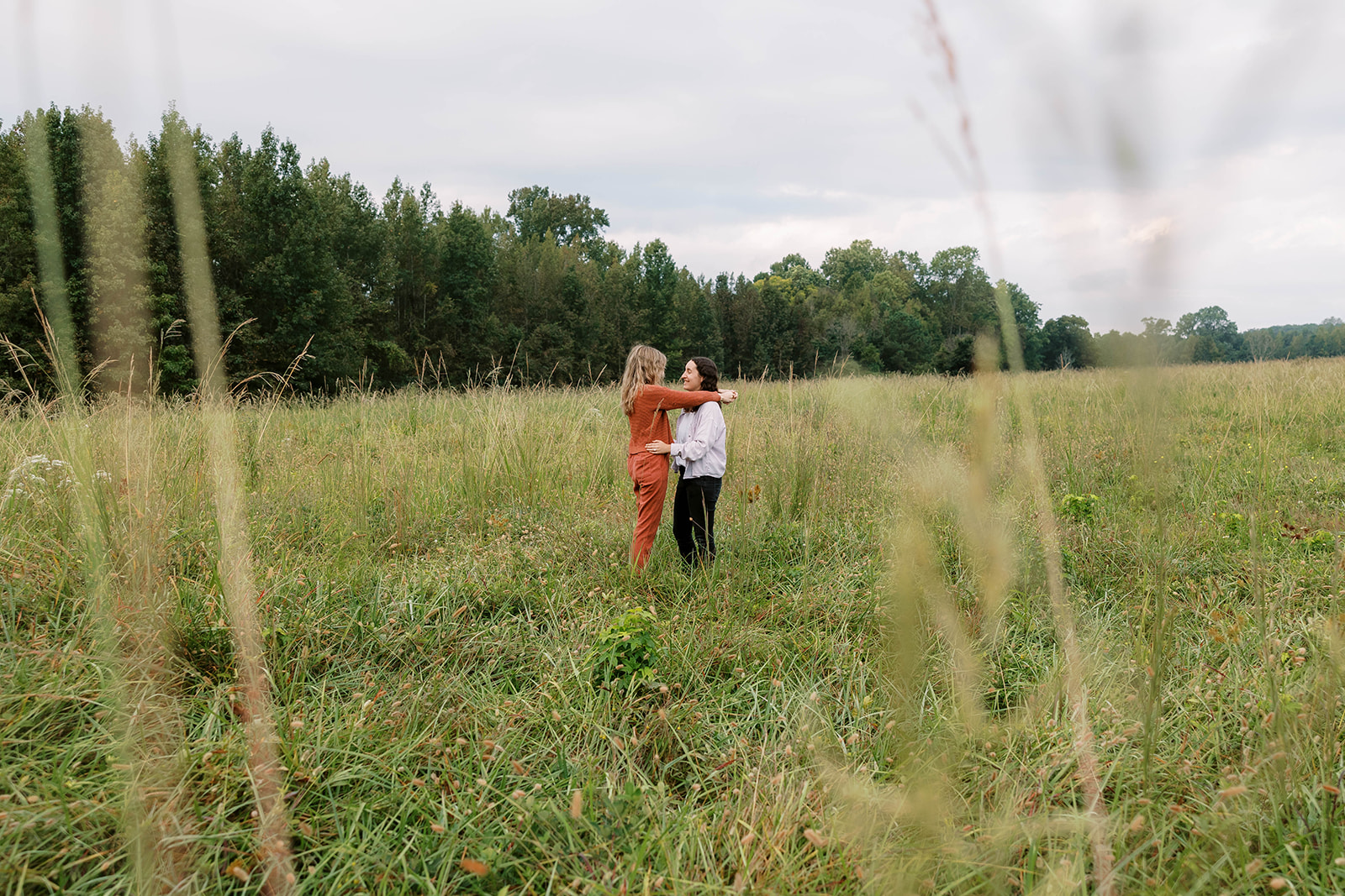 Atlanta LGBTQ+ engagement session with two lesbians holding each other in a filed. Both are wearing casual outfits and they have their arms wrapped around each other.